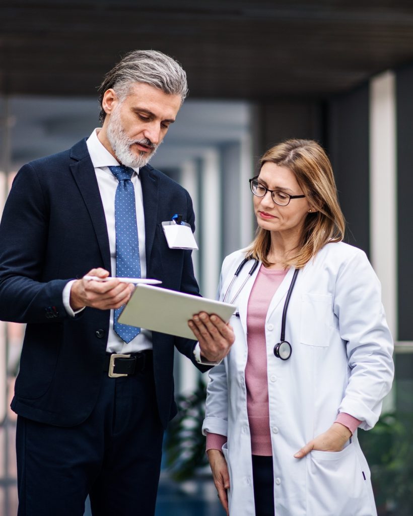 Pharmaceutical sales representative with tablet talking to doctor